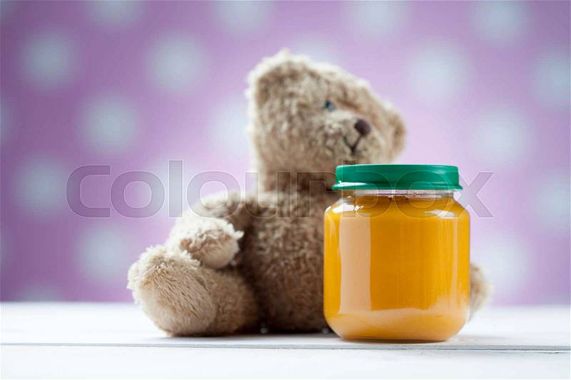 Teddy bear with jar of food on wooden table, stock photo