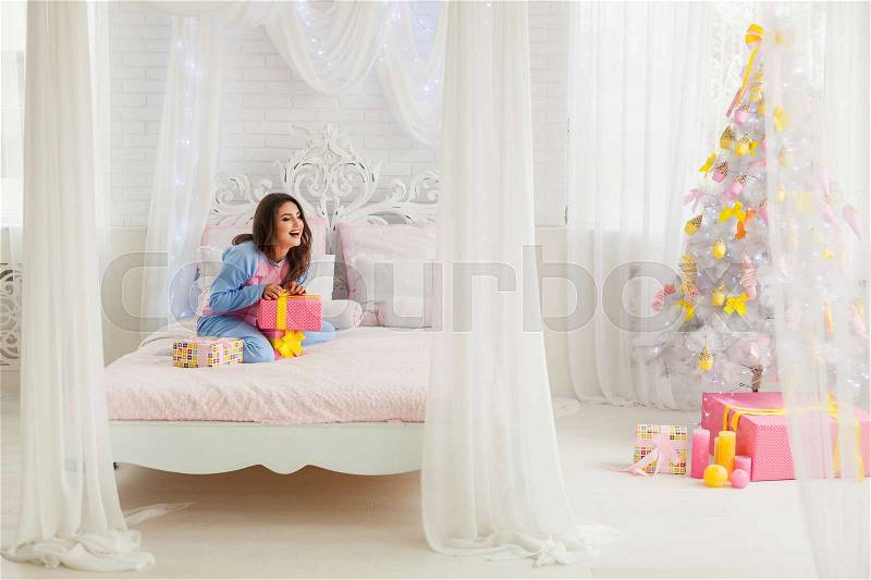 Laughing model opening presents in bed near christmas tree, stock photo