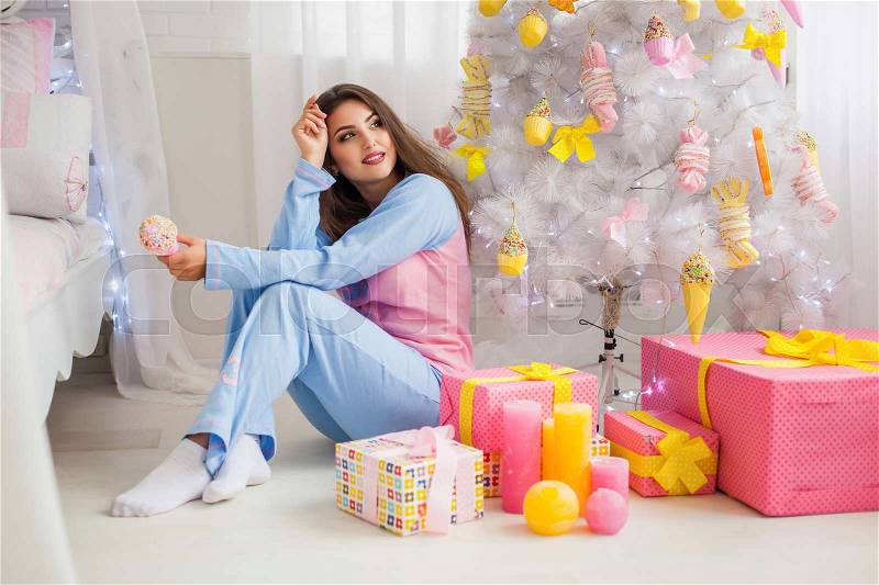 Young girl in pyjamas with christmas presents near fir-tree, stock photo