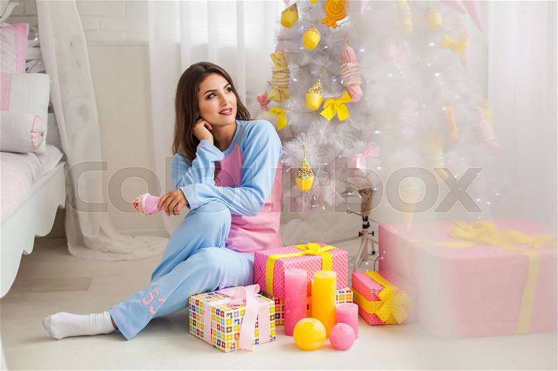 Young woman in pyjamas with christmas presents near fir-tree, stock photo