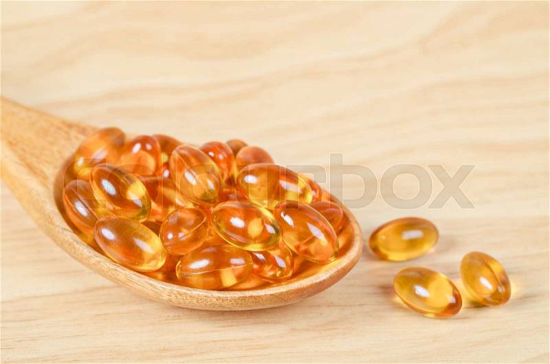 Cod liver oil omega 3 gel capsules in wooden spoon on wooden background, stock photo