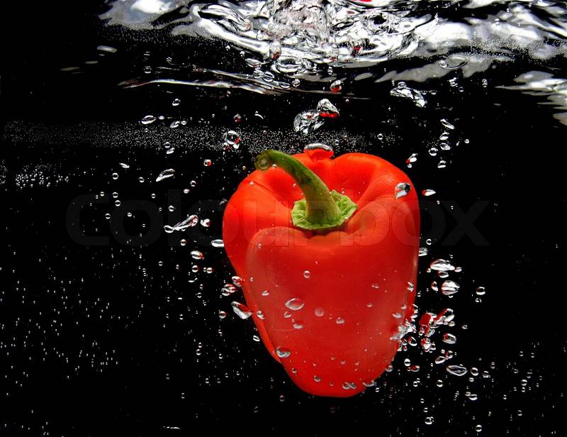 Red pepper splashing in water over black, stock photo