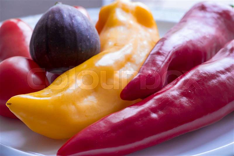Red and yellow sweet pepper, red tomatoes and a deep violet fig served on a white plate, stock photo