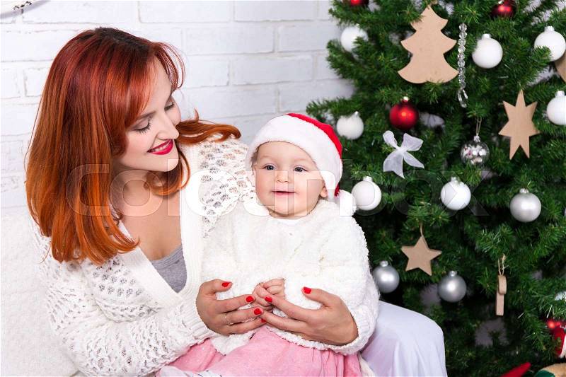 Young mother and little daughter sitting in front of Christmas tree, stock photo
