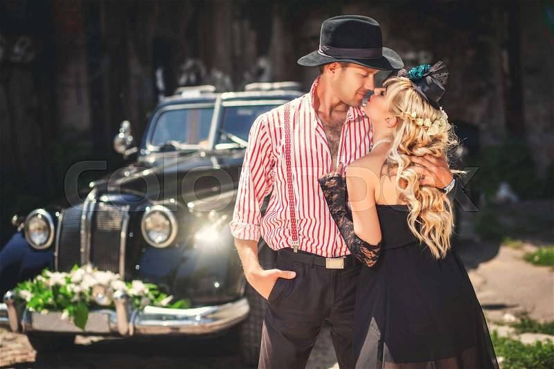 Kissing couple standing near old-fashioned car outdoors, stock photo