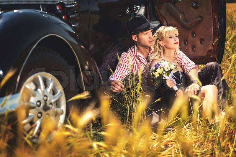 Woman with bouquet and man sitting together near old-fashioned car, stock photo