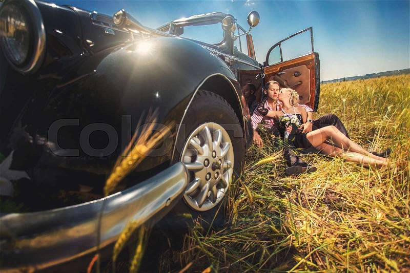 Couple in love kissing near old-fashioned car on wheat field, stock photo