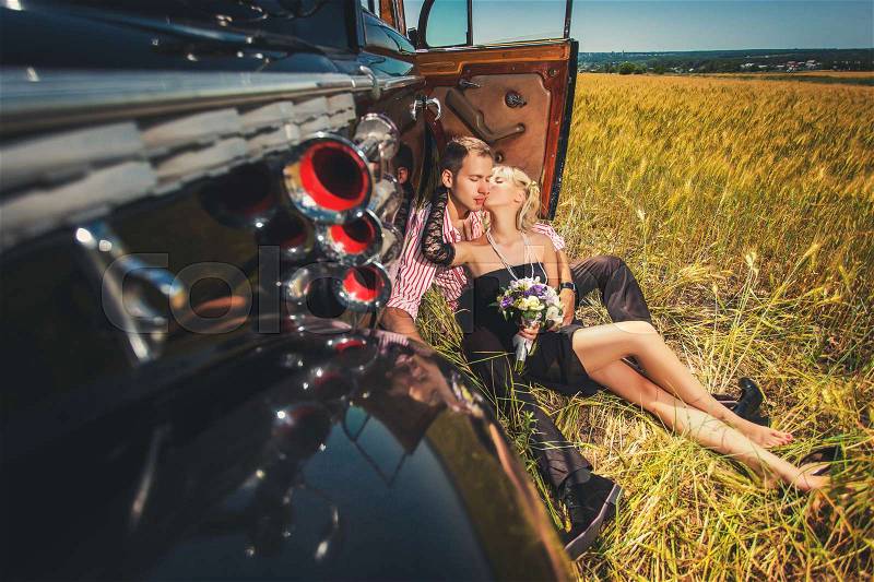 Happy couple in love kissing near old-fashioned car on wheat field, stock photo