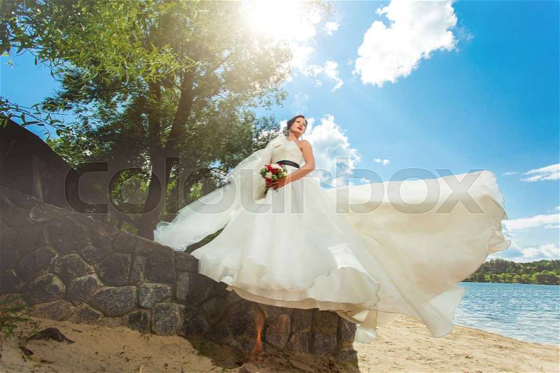 Bride with flowing dress standing on decorative stone fence, stock photo