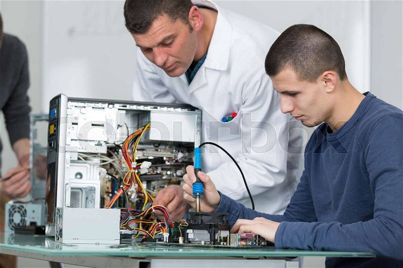 Male teacher assisting a young man in fixing computer, stock photo