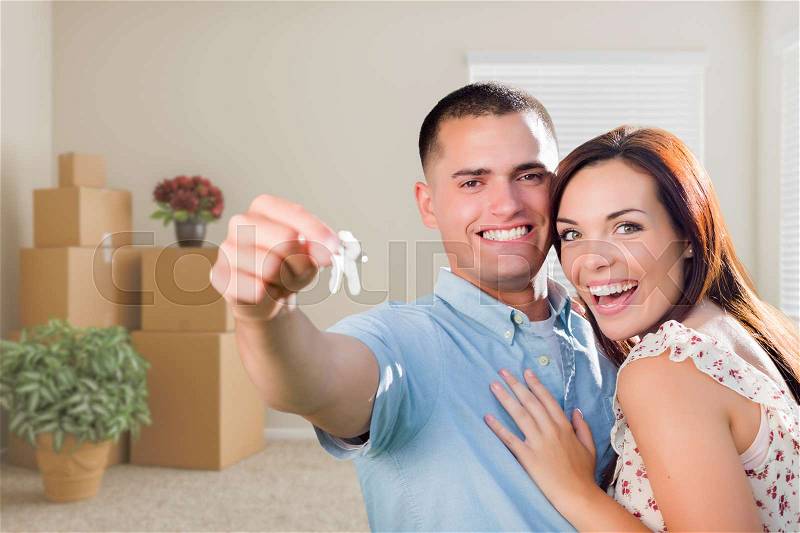 Happy Young Military Couple with House Keys in Empty Room with Packed Moving and Potted Plants, stock photo