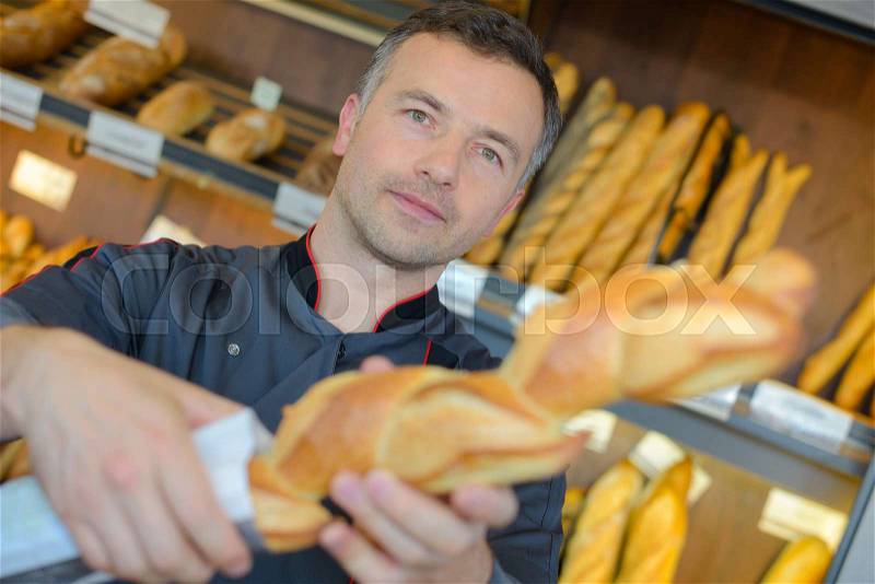 Baker selling fresh bread baguettes in bakery, stock photo