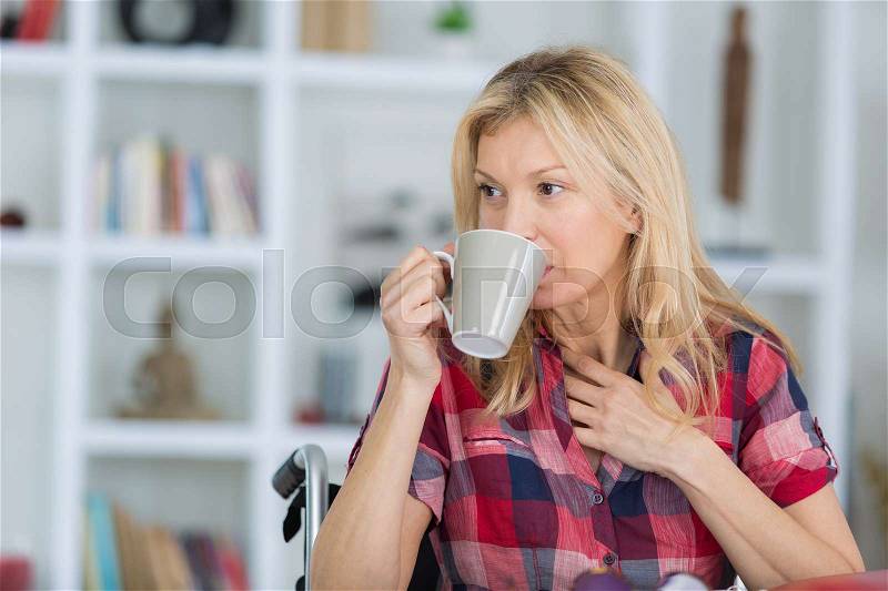 Woman sitting on wheelchair holding tea mug, stock photo