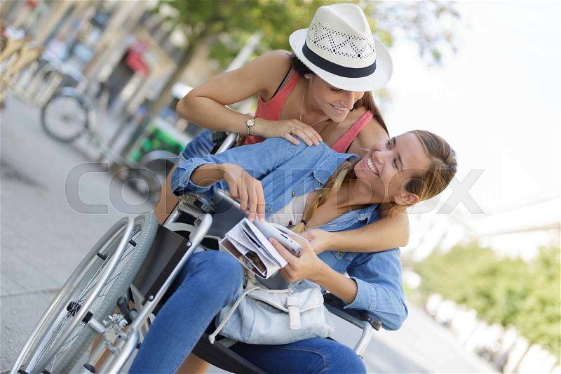 Two friends visiting foreign city one sitting in wheelchair, stock photo