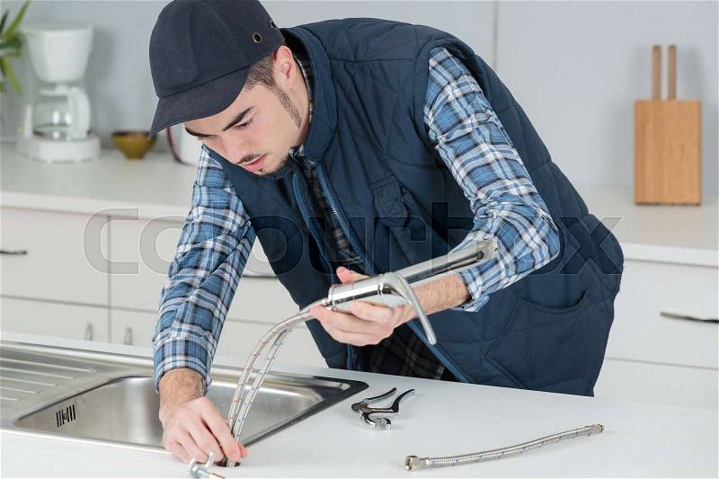 Young craftsman repairing tap in a kitchen, stock photo