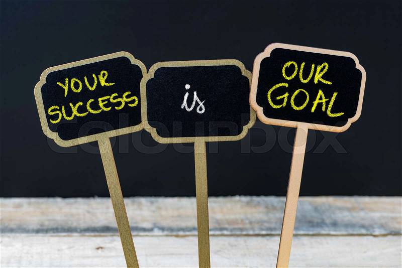 Concept message YOUR SUCCESS IS OUR GOAL written with chalk on wooden mini blackboard labels, defocused chalkboard and wood table in background, stock photo