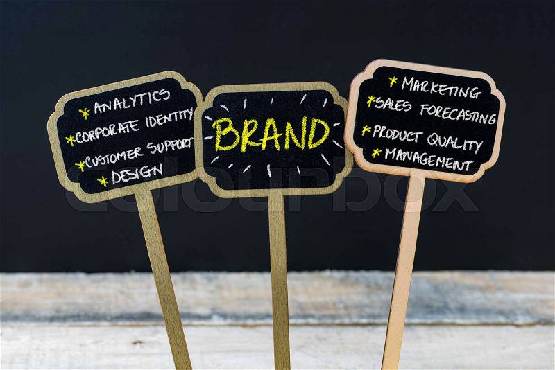 Concept message BRAND written with chalk on wooden mini blackboard labels, defocused chalkboard and wood table in background, stock photo