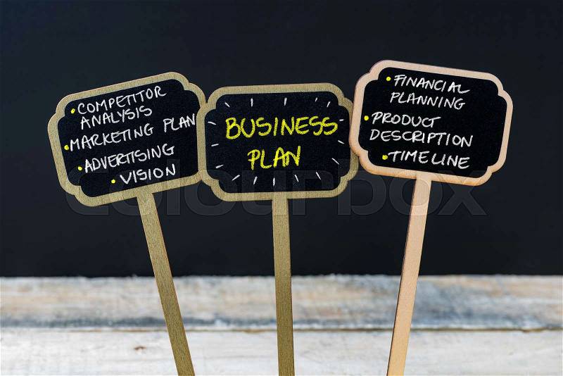 Concept message BUSINESS PLAN written with chalk on wooden mini blackboard labels, defocused chalkboard and wood table in background, stock photo