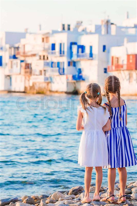 Little kids at Little Venice the most popular tourist area on Mykonos island, Greece. Back view of beautiful girls look at Little Venice background, stock photo