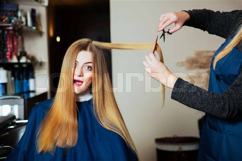 Stylist making hairstyle with scissors and comb in hands. Young woman with long hair, stock photo
