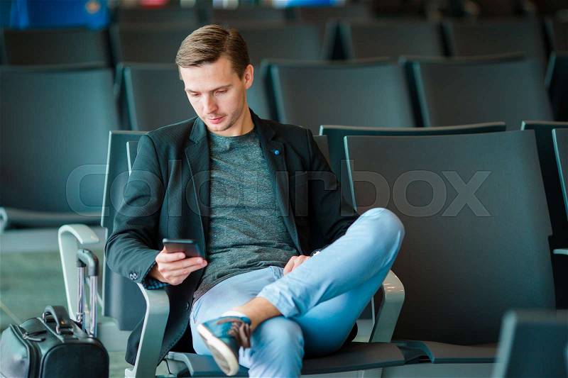 Urban business man talking on smart phone traveling inside in airport. Casual young businessman wearing suit jacket. Handsome male model. Young man with cellphone at the airport while waiting for boarding, stock photo