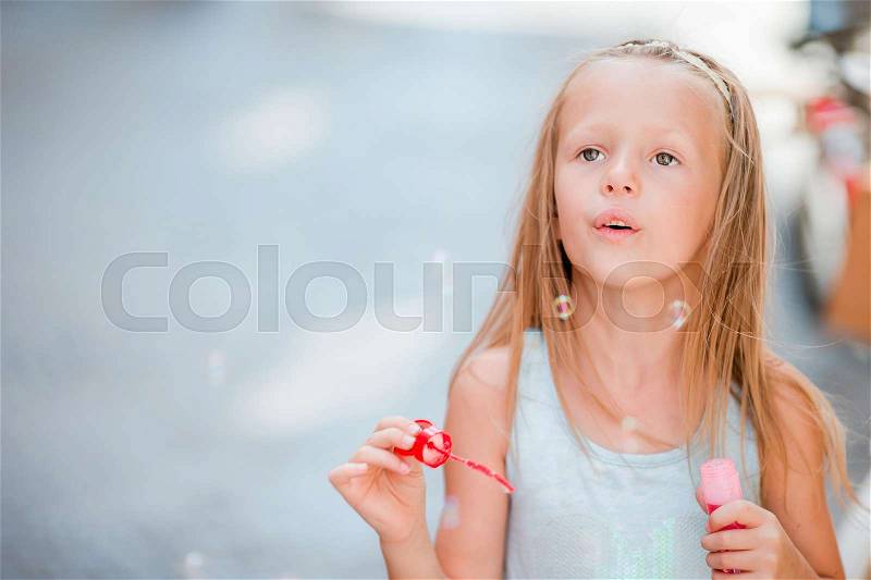 Adorable little girl outdoors blowing soap bubbles in european city. Portrait of caucasian kid enjoy summer vacation in Italy, stock photo