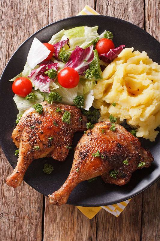 Baked duck leg, mashed potatoes and fresh salad mix close-up on a plate. Vertical view from above\, stock photo