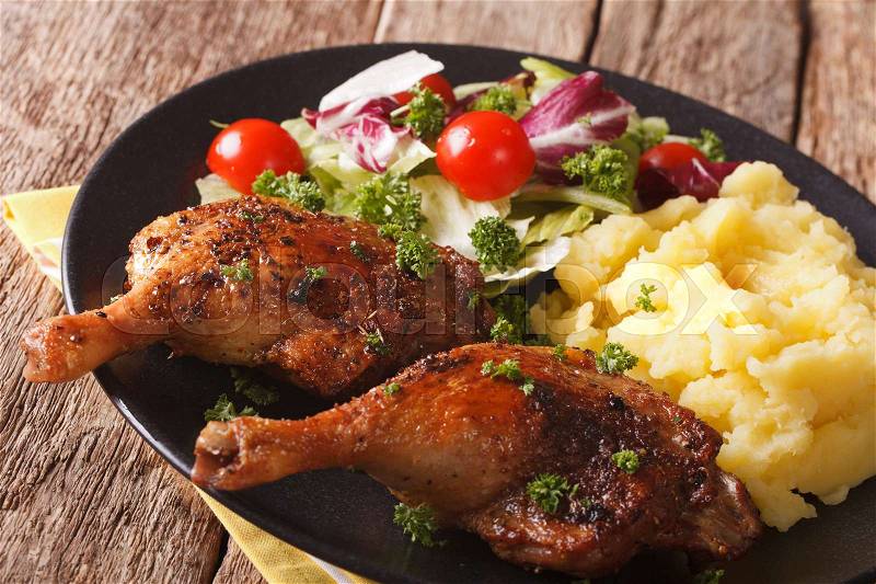Baked duck leg with mashed potatoes garnish and salad mix close-up on a plate. Horizontal , stock photo