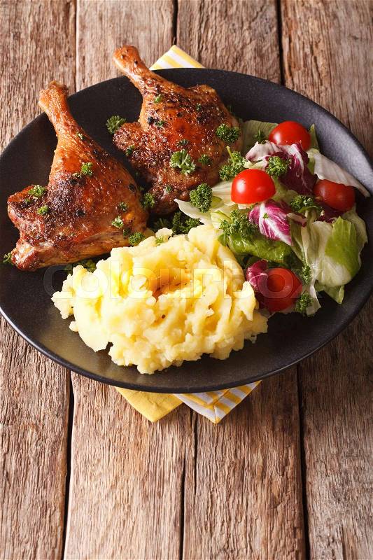 Baked duck leg with mashed potatoes garnish and salad mix close-up on a plate. vertical\, stock photo