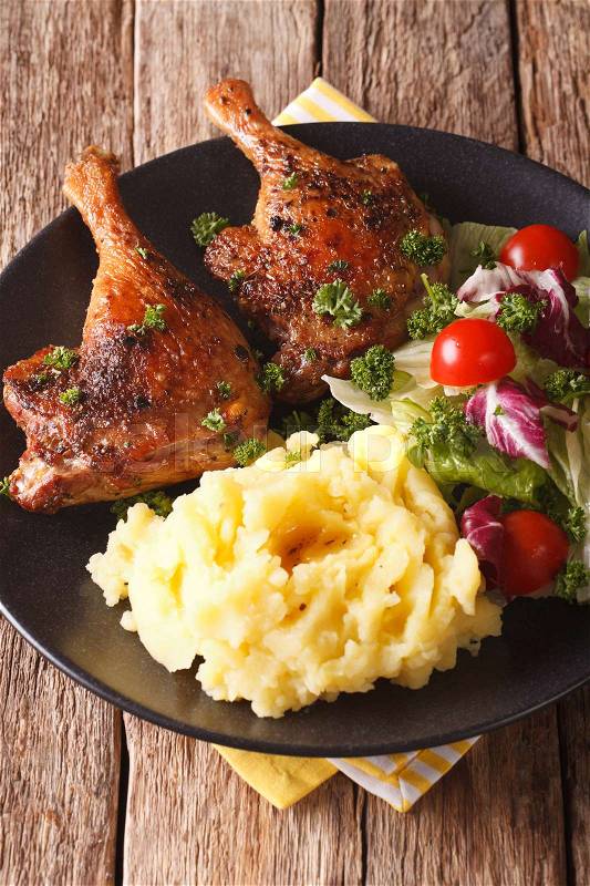 Roasted duck leg with mashed potatoes garnish and salad mix close-up on a plate. vertical\, stock photo