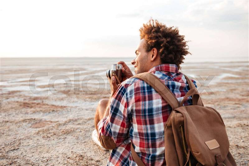 Back view of happy african young man taking pictures on the beach, stock photo