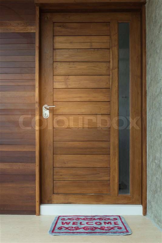Welcome door mat infront of teak wooden door background, stock photo