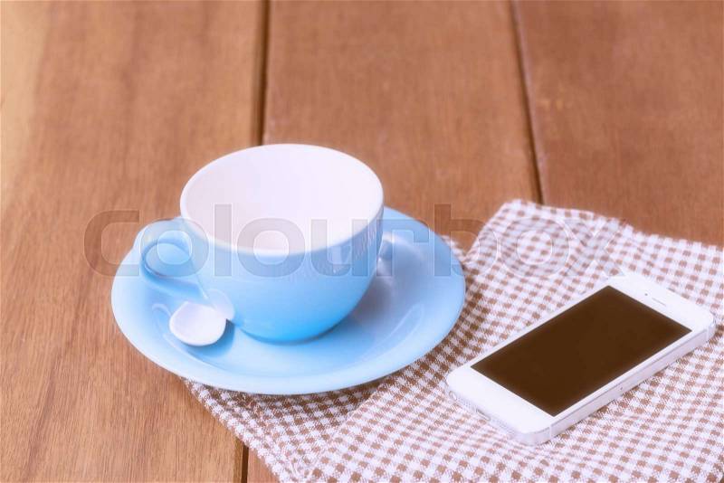 Blue coffee cup and smart phone on wooden table, stock photo