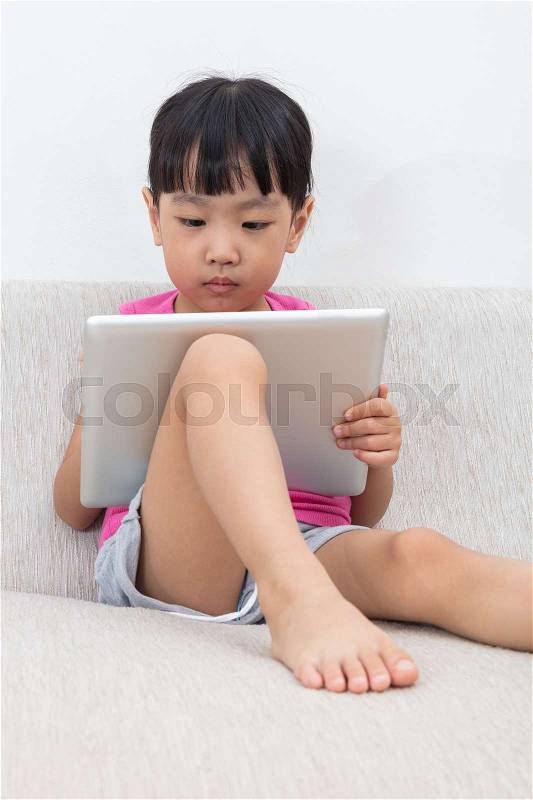 Asian Chinese little girl sitting on the sofa with tablet in the living room, stock photo