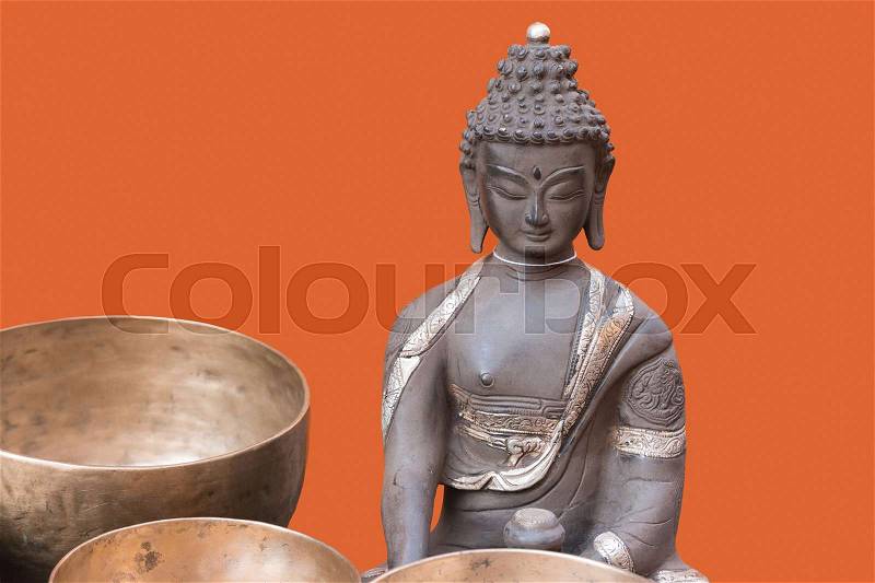 Old bronze sculpture (statue) of Buddha with bronze bowls in front of the figure isolated on the orange background, stock photo