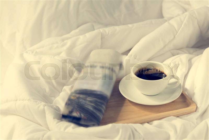 Cup of coffee and newspaper with wooden tray on bed background, stock photo