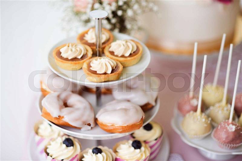 Tarts with meringues, glazed cream puffs or profiterole and cupcakes on cakestand. Cake pops on plate, stock photo