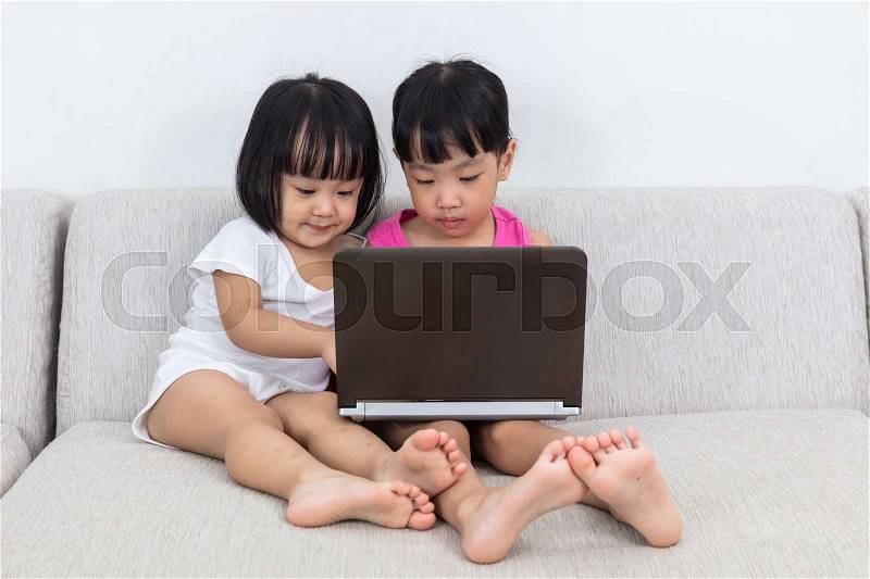 Asian Chinese little sisters playing computer on the sofa in the living room, stock photo
