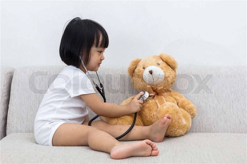 Asian Chinese little girl checking up a teddy bear on the sofa, stock photo