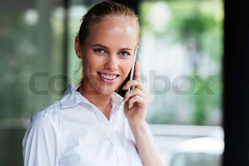 Close up potrait if a smiling businesswoman talking on the phone and looking at camera, stock photo