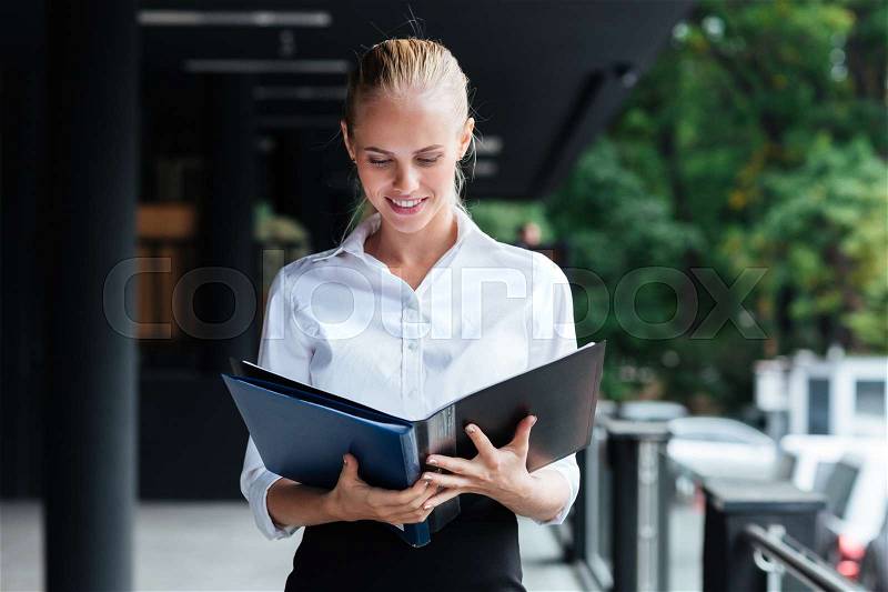 Happy young business woman standing and holding folders outside, stock photo