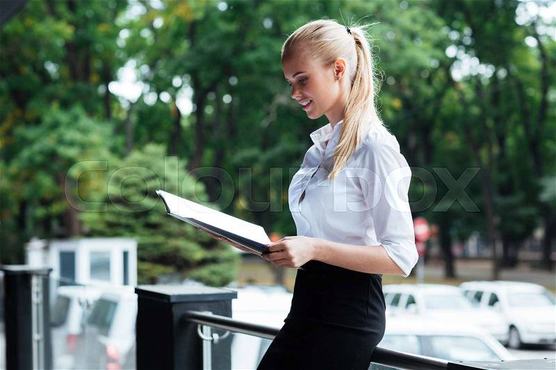 Happy young business woman standing and holding folders outside, stock photo