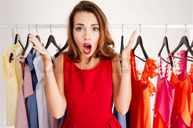 Close up portrait of a confused lovely woman in red dress choosing what to wear isolated on a white background, stock photo