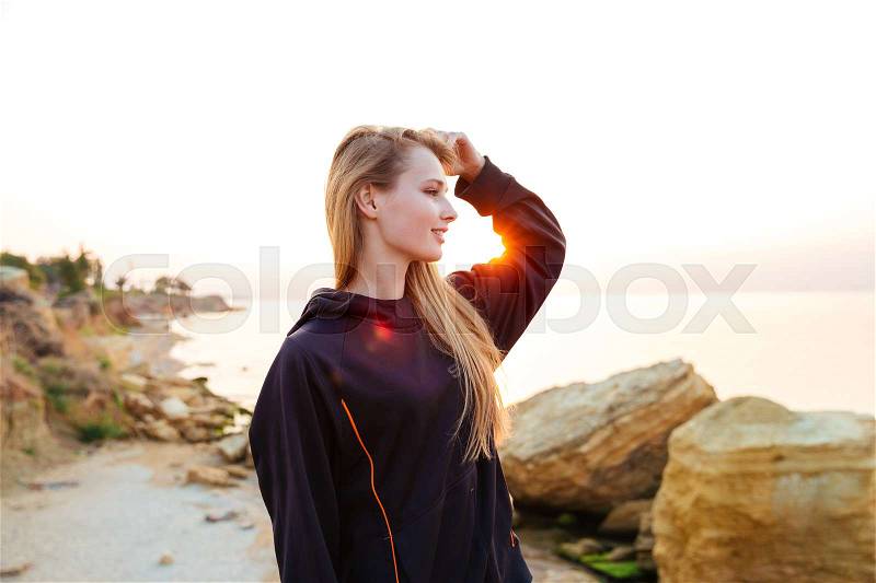 Young runner woman resting after jogging training on beach at sunset, stock photo