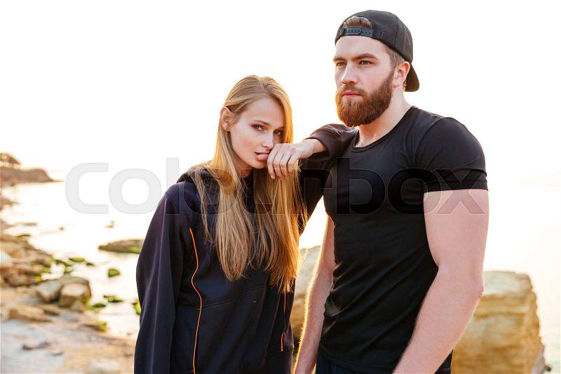 Beautiful young sports couple resting after workout while standing at the beach, stock photo