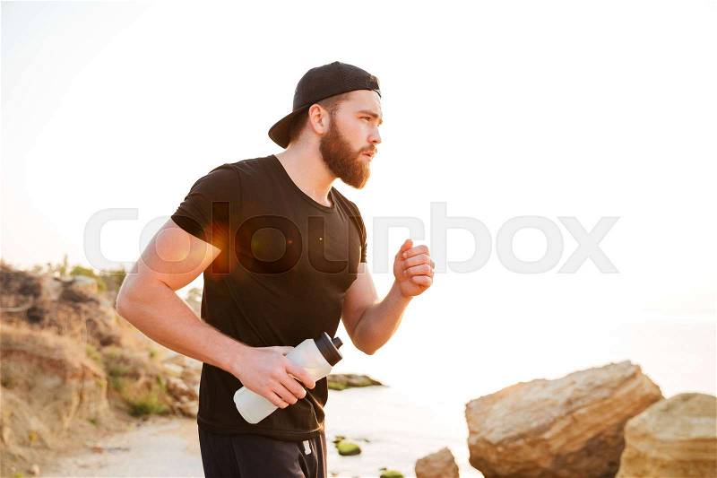 Side view portrait of a bearded sports man running outdoors near sea, stock photo