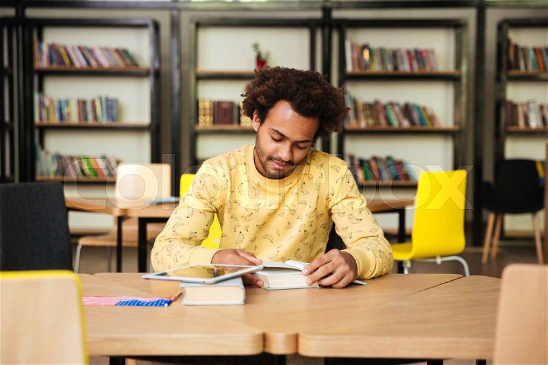 Concentrated african american young man reading book and learning in library, stock photo