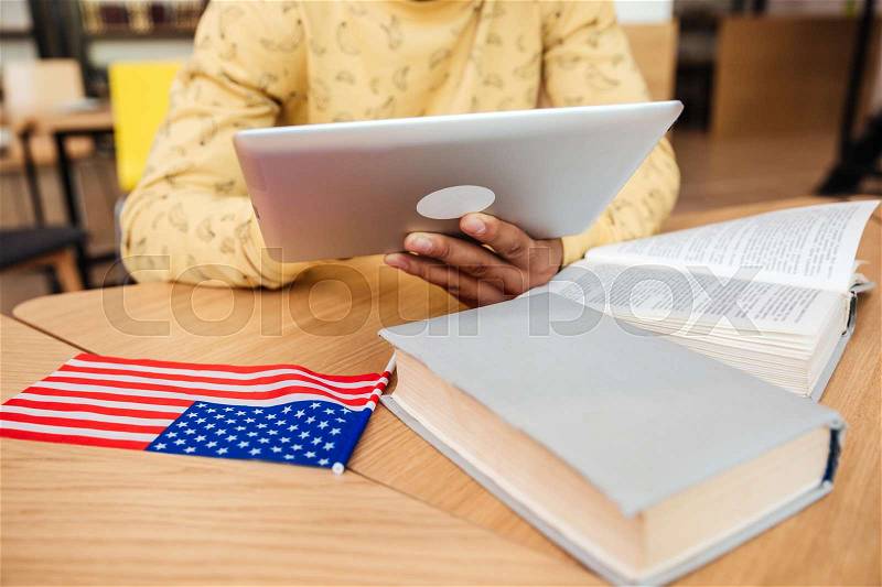 Closeup of african young man sitting and learning with book and tablet at the table, stock photo