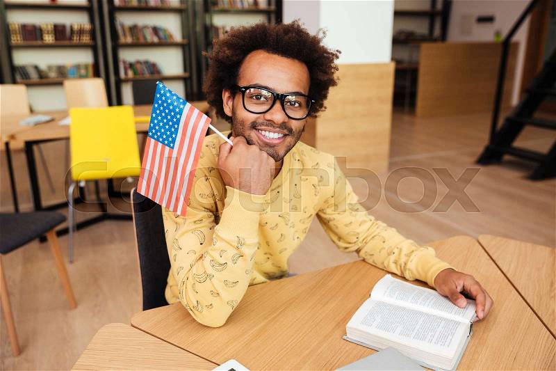 Cheerful man holding flag of United States and reading book, stock photo