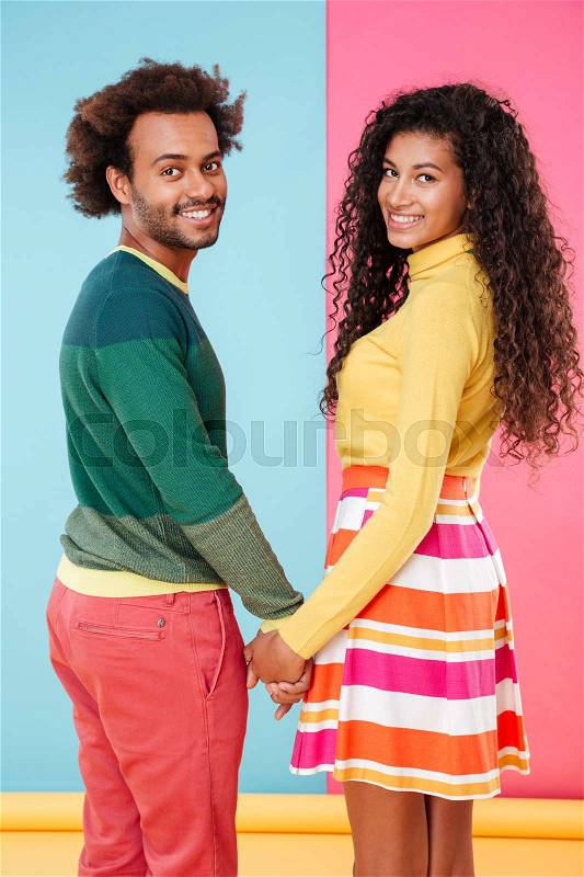 Happy african young couple holding hands and looking back over bright colorful background, stock photo